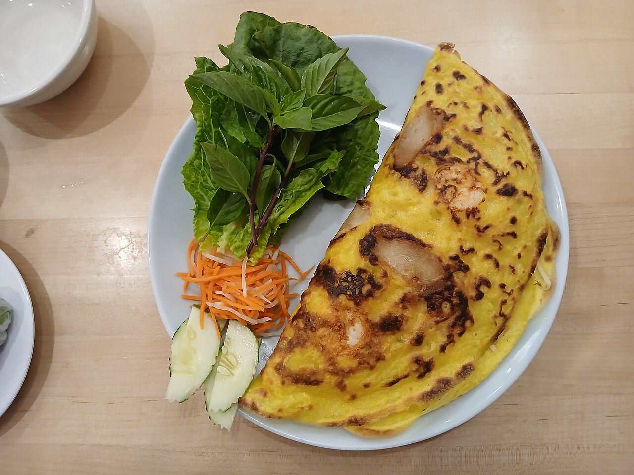 Chiếc bánh xèo vàng giòn ăn kèm rau sống và dưa leo